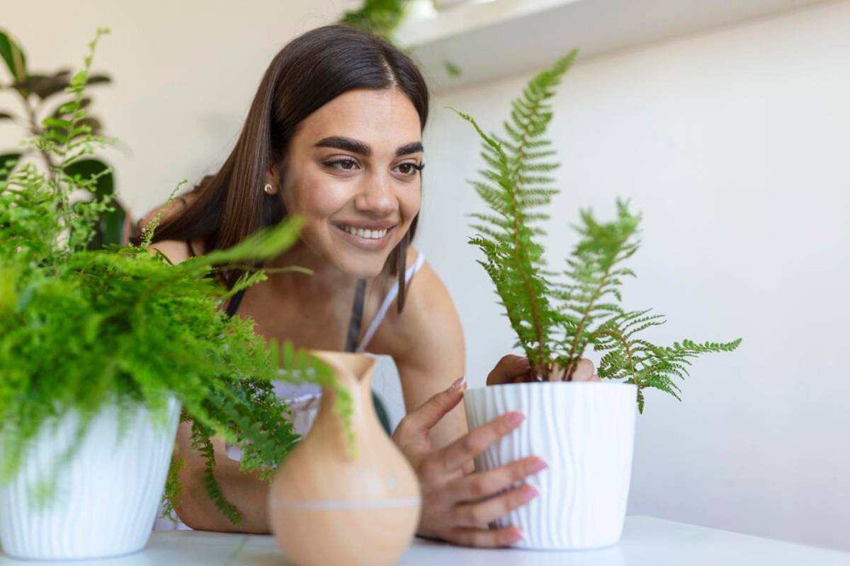 Young woman smiling and arranging ferns in white pots on a table.