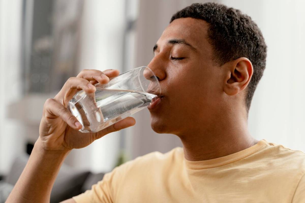 A young man drinking water from a clear glass.