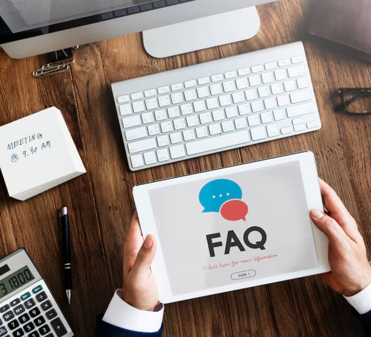 A person holding a tablet displaying FAQ with a desktop setup in the background.