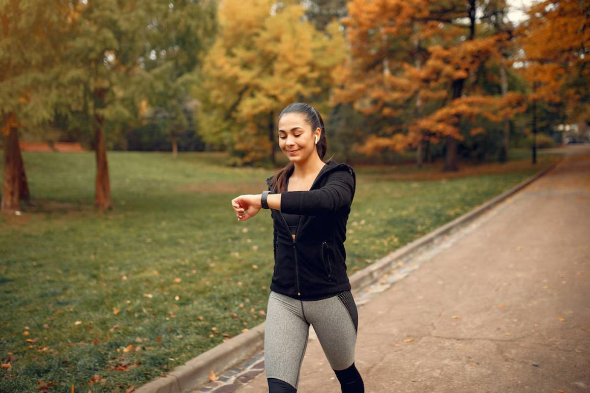 Woman checking her smartwatch while walking on a park path in autumn.