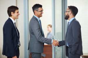 Two people in business attire shaking hands against a clear blue sky.