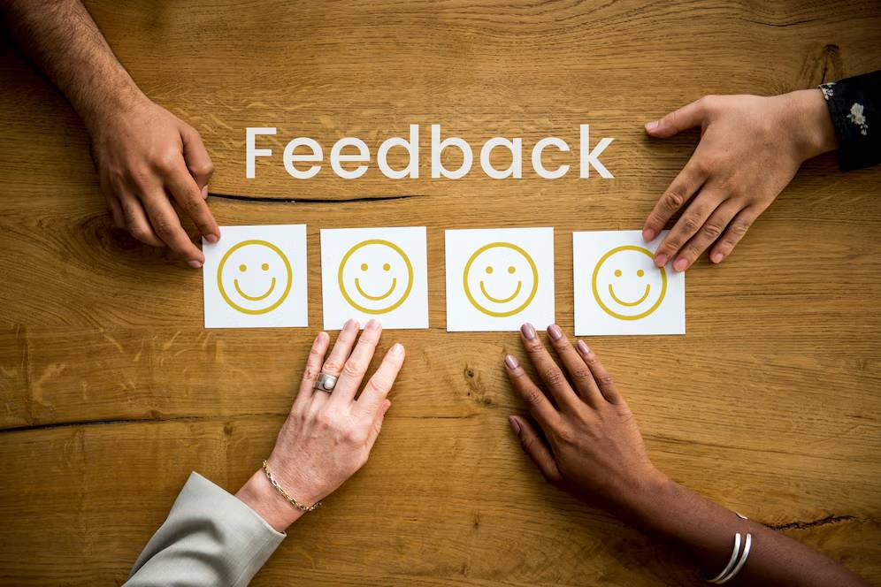 Four diverse hands point at smiling face icons on a table labeled Feedback.