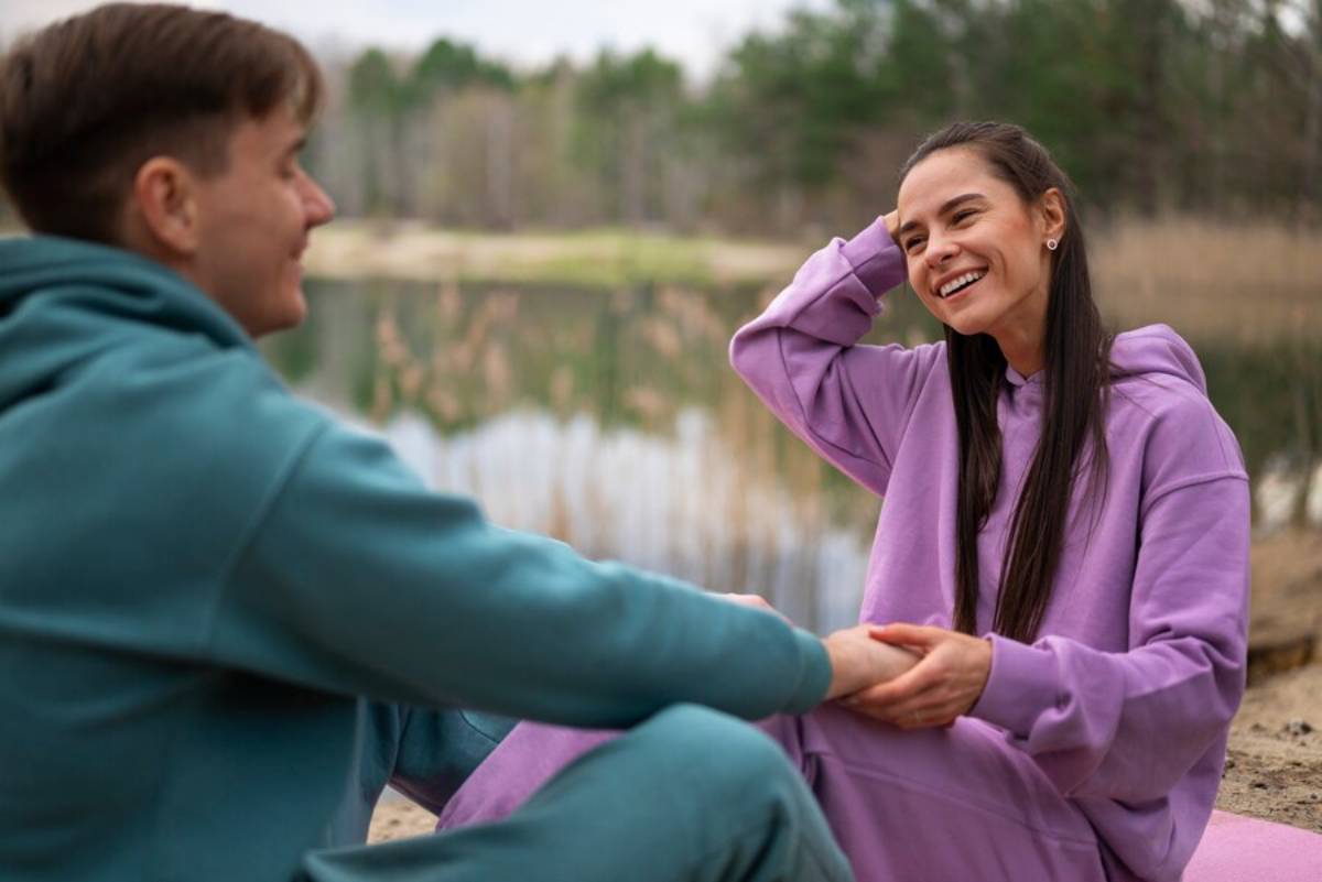 Young couple smiling and holding hands by a serene lakeside, surrounded by a forest.