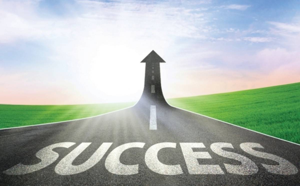 Asphalt road with the word SUCCESS leading to an arrow-shaped horizon over green fields under a clear sky.