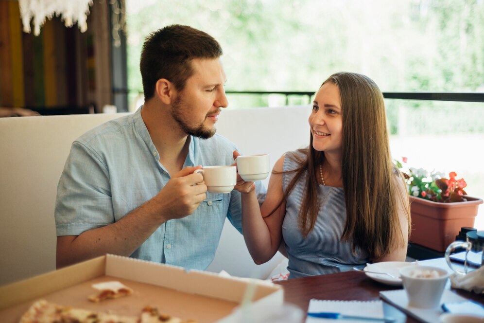 A young couple enjoying coffee and smiling at each other in a well-lit cafe setting.