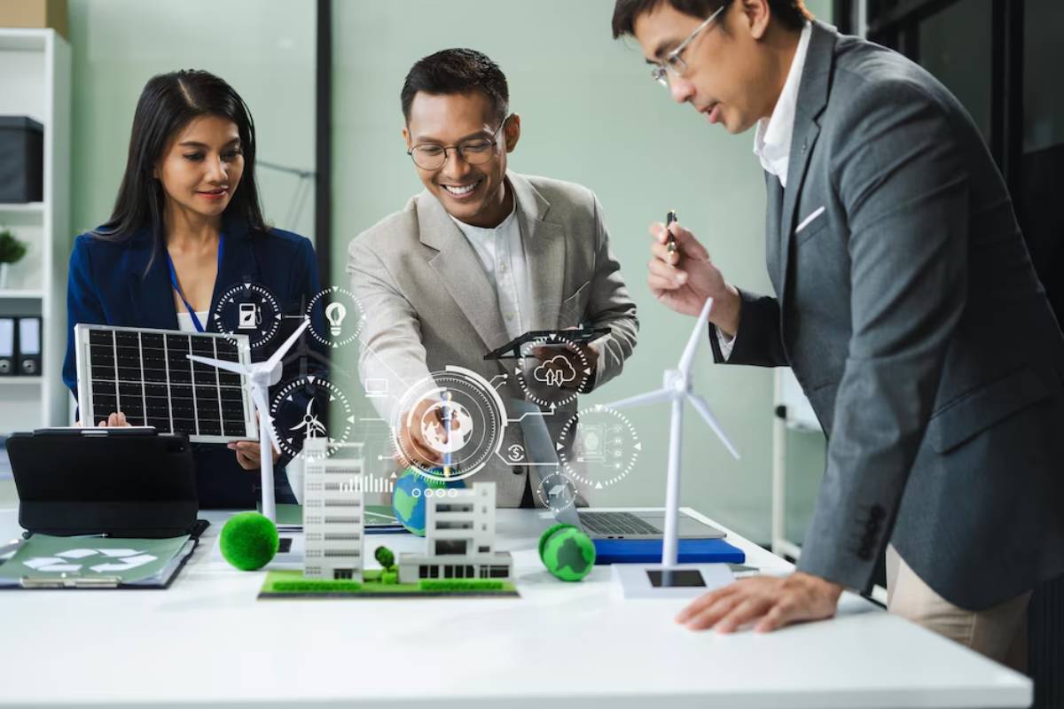 Three professionals discuss renewable energy projects, handling solar panels and wind turbine models in an office setting.