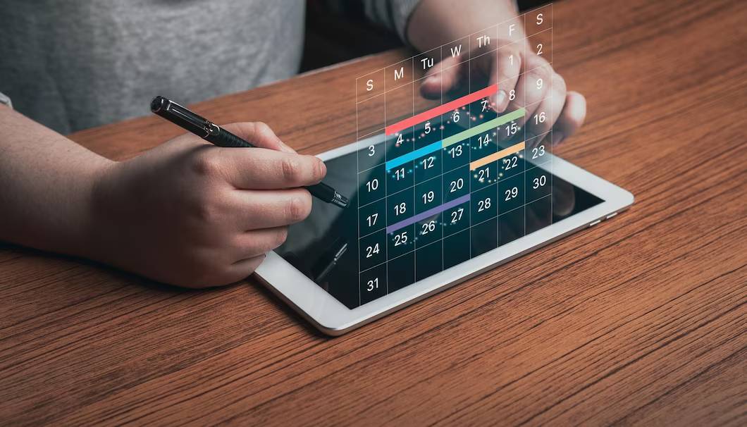 Person using a stylus on a tablet to interact with a digital calendar interface.