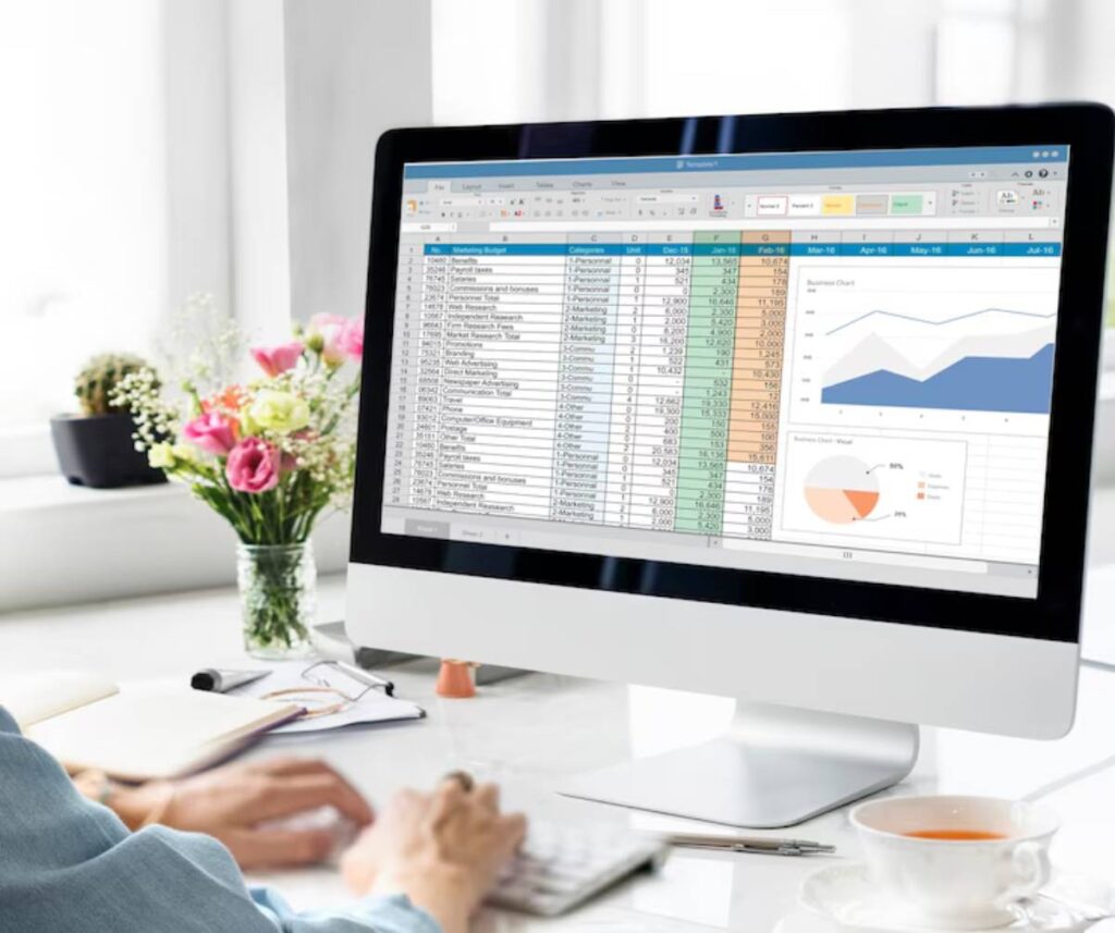 Person working on a spreadsheet on a computer with graphs visible, in a bright office setting.