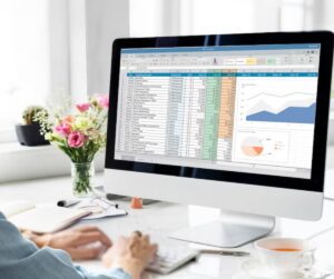 Person working on a spreadsheet on a computer with graphs visible, in a bright office setting.
