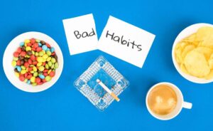 A conceptual image of Bad Habits with candy, chips, cigarettes, and coffee on a blue background.