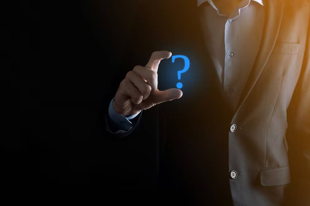 A man in a suit holding a glowing question mark icon in his hand on a dark background.