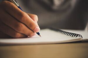 Close-up of a hand writing with a blue pen in a spiral notebook.