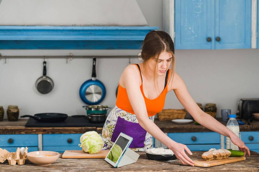 Young woman preparing food in a rustic kitchen, reaching for a cucumber on a wooden countertop.