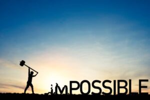 Silhouette of a man swinging a hammer at the word IMPOSSIBLE with the breaking away, at sunset.